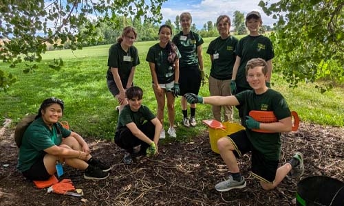 Person sitting on ground in grassy area with a group of teen volunteers