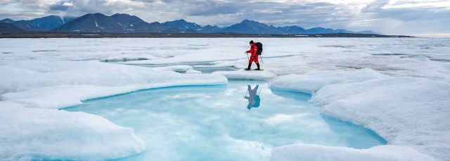 Person hiking with snow and water in the foreground, mountains in the distance